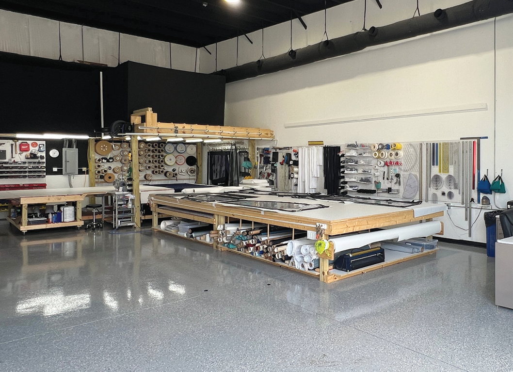 Bright workshop featuring organized materials and tools on shelves, with a large work table at the center showcasing various marine fabrication supplies.