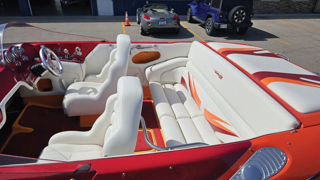 Boat interior featuring white leather seating with orange accents, a chrome steering wheel and polished dashboard gauges.