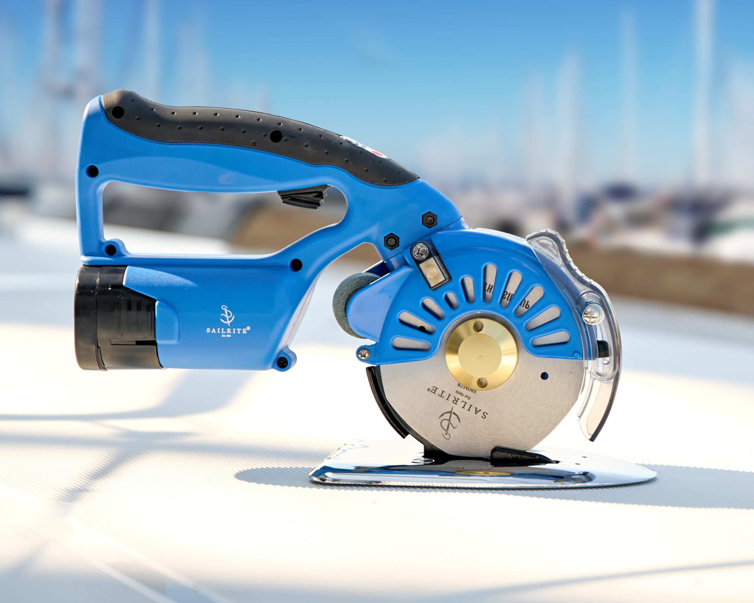 Blue cordless rotary cutter with a silver blade, set against a blurred marine background.