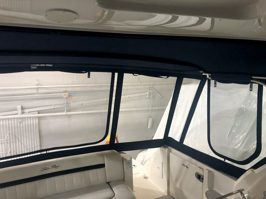 Interior view of a marine vessel featuring a beige seat with Sea Ray branding, black window frames and a dark canopy overhead.