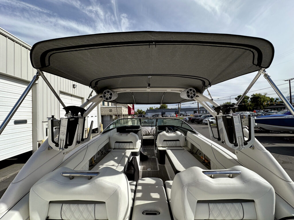 Open boat interior with white seating, a gray canopy overhead and a visible control console. Background features vehicles and buildings.