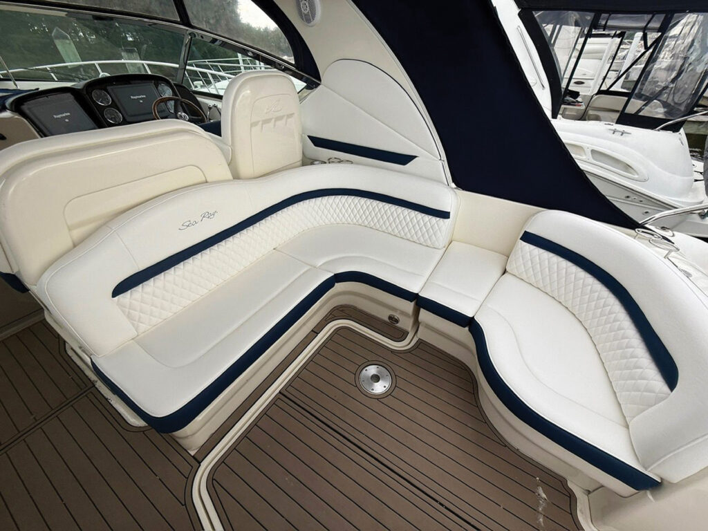 Curved white boat seating with navy blue accents and diamond-quilted patterns, set against a wooden deck and a cabin backdrop.