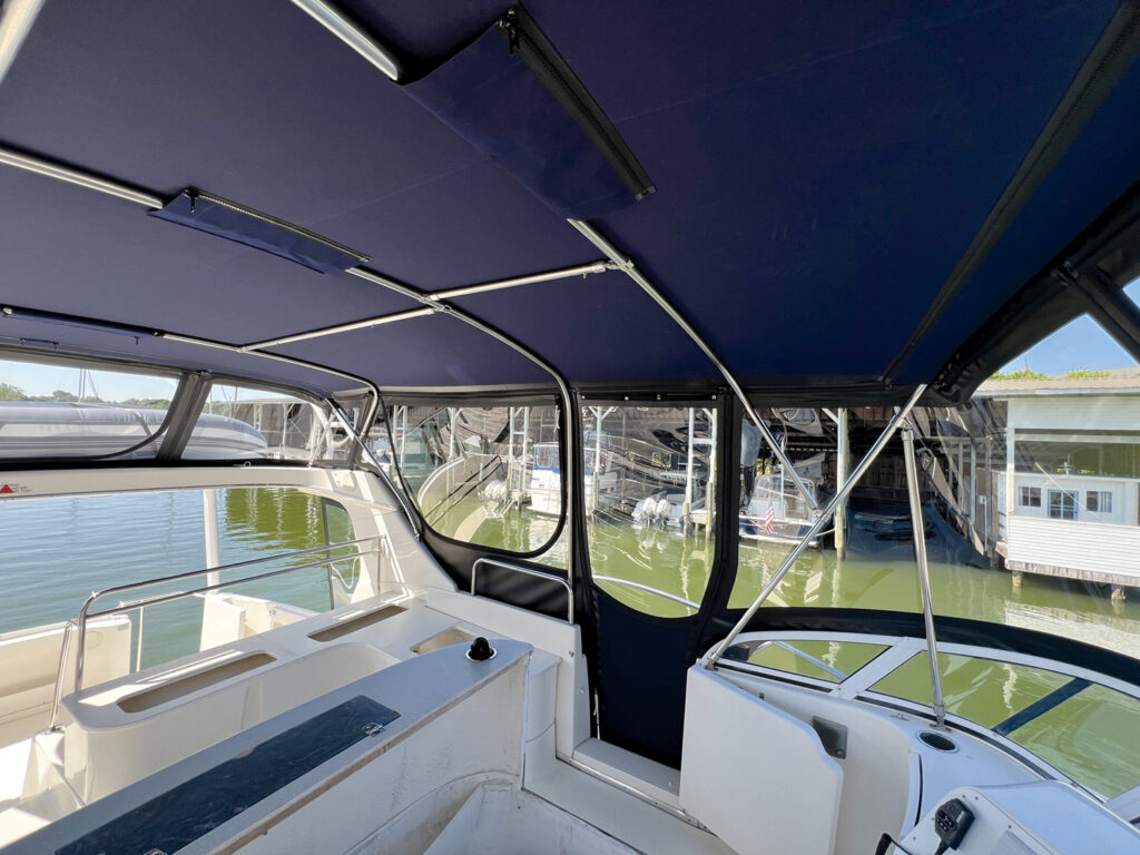 Blue canopy covering the interior of a boat, with white seating and a view of docks and boats reflecting on green water.