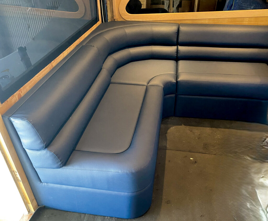 Curved navy blue seating with cushioned surfaces in a cozy marine interior, set against wooden accents and a reflective window.