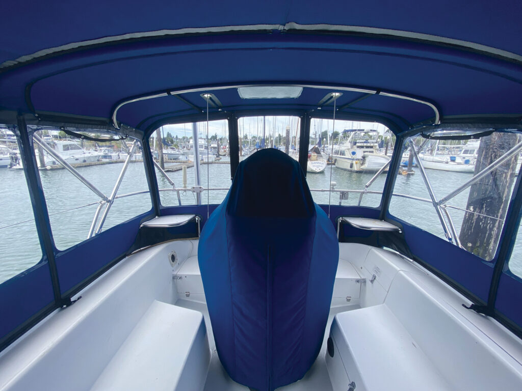 Interior view of a boat with a blue canopy and seat cover, overlooking a marina filled with boats and water.