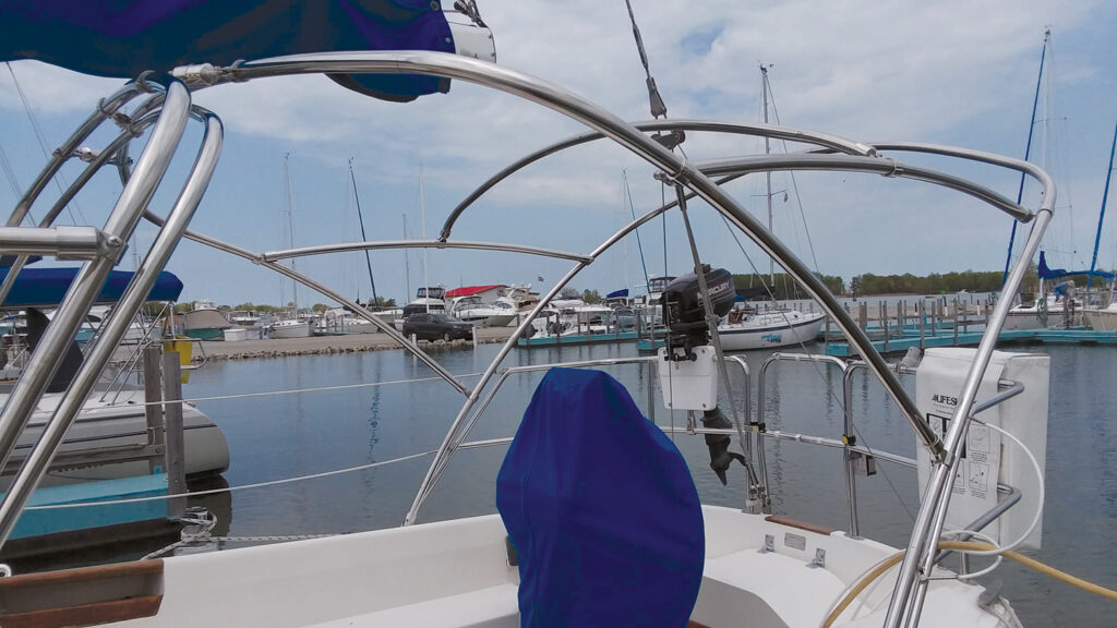 A view from a boat cockpit featuring stainless steel frames, a blue cover and several moored boats in a calm marina.