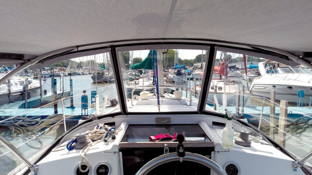 View from the helm of a boat, showing a marina filled with various boats and masts, with a clean, bright interior and ropes in the foreground.