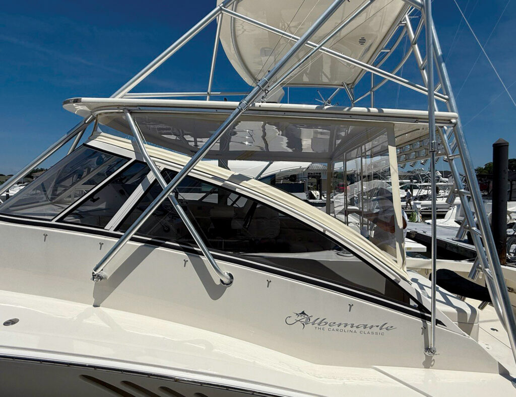 Sport fishing boat with a white hull, large windshield and stainless steel frame, docked among other boats under a clear blue sky.