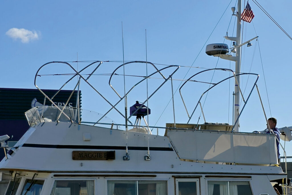 Adjustable framework atop a boat named "Maggie B," with a man adjusting equipment against a clear blue sky and visible flag.