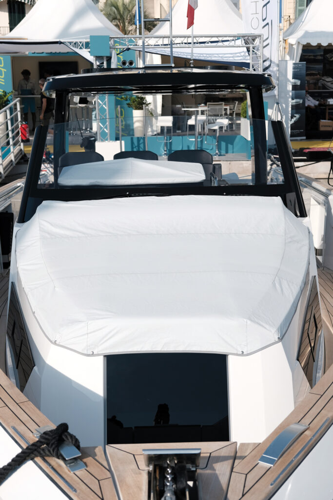 White cover drapes over a boat's cockpit, showcasing polished wood accents and a glossy black windshield in a sunny setting.