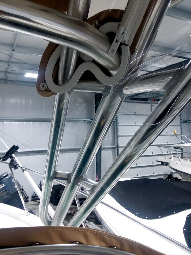 Close-up of polished stainless steel tubing intersecting in a boat's framework, with boats and a garage background visible.