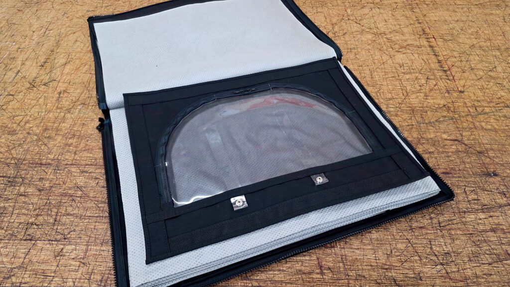 Black zippered binder opened to reveal a transparent pouch on a textured surface, with a light gray interior and black trim.