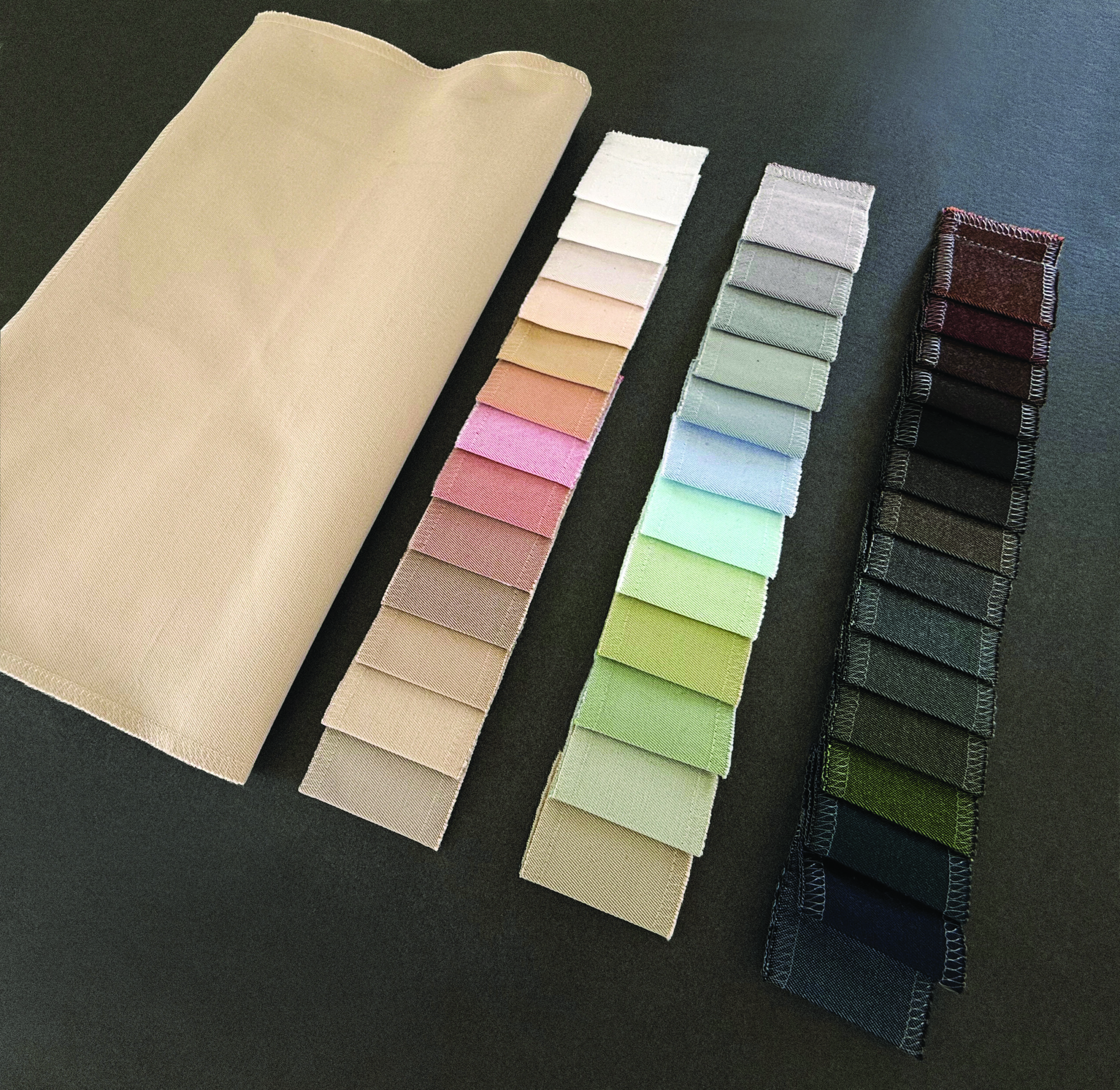 A folded beige fabric swatch next to rows of color samples in pastel and darker shades, all displayed on a dark background.