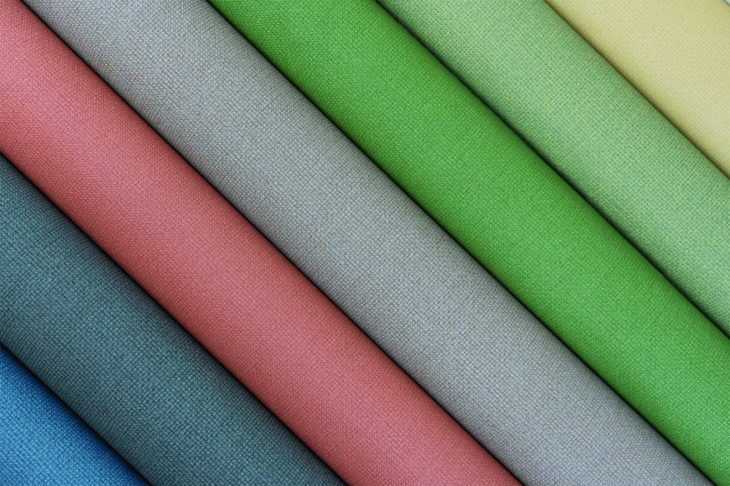 Eight folded fabric swatches in pastel shades of pink, blue, green, grey and yellow arranged diagonally, showcasing texture and color variation.
