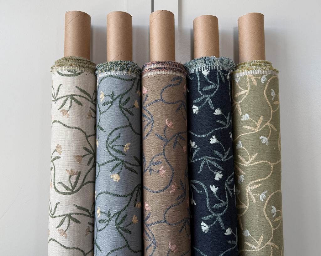Five fabric rolls display various floral patterns in soft colors, including cream, blue, green, navy and olive, showcasing a nature-inspired theme.