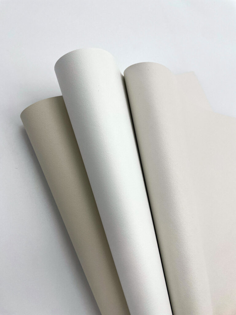 Three rolls of textured fabric in varying shades of off-white and cream, arranged slightly overlapping on a light background.