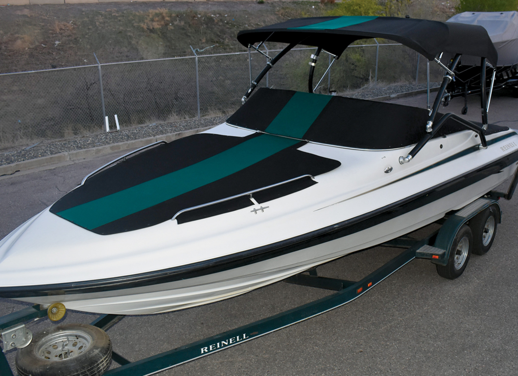 MF_FeaturedImages_254x184px3 White boat with a black and green canopy and matching accents, parked on a trailer against a background of fencing and hills.