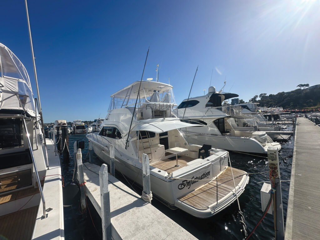 White yachts moored at a dock under a clear blue sky, with masts and a spacious deck visible on the prominent vessel.