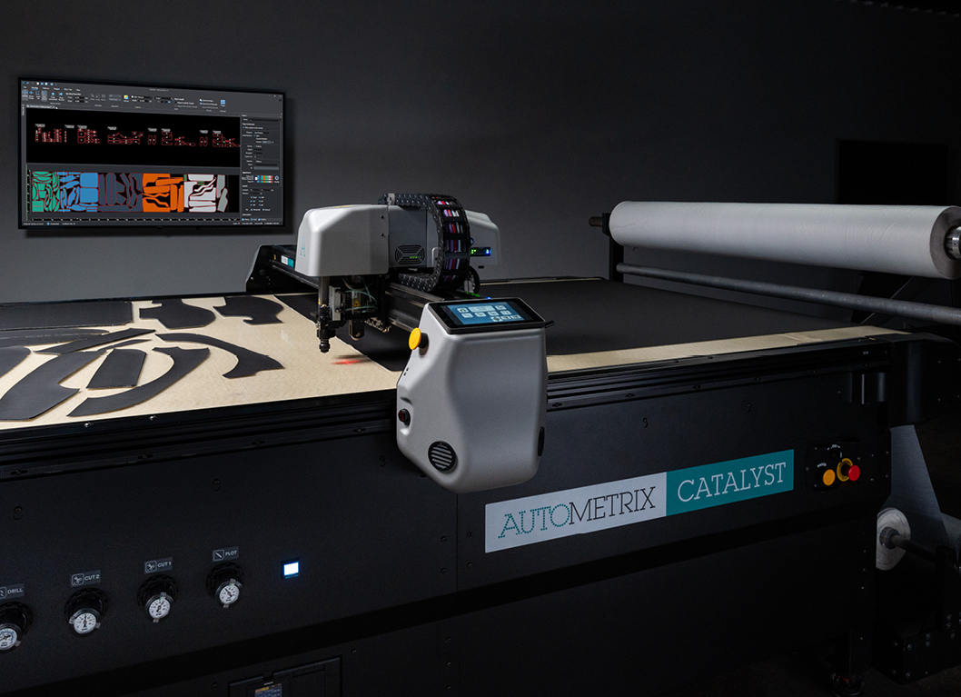 MF_FeaturedImages_254x184px1 A digital cutting machine on a work table with colorful fabric designs and a screen displaying design software in the background.