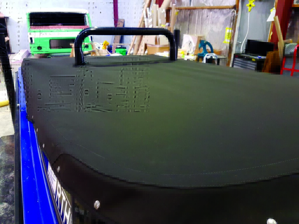 Black marine fabric stretched over a blue boat, showcasing a sturdy black handle mounted on top, with tools and materials in the background.