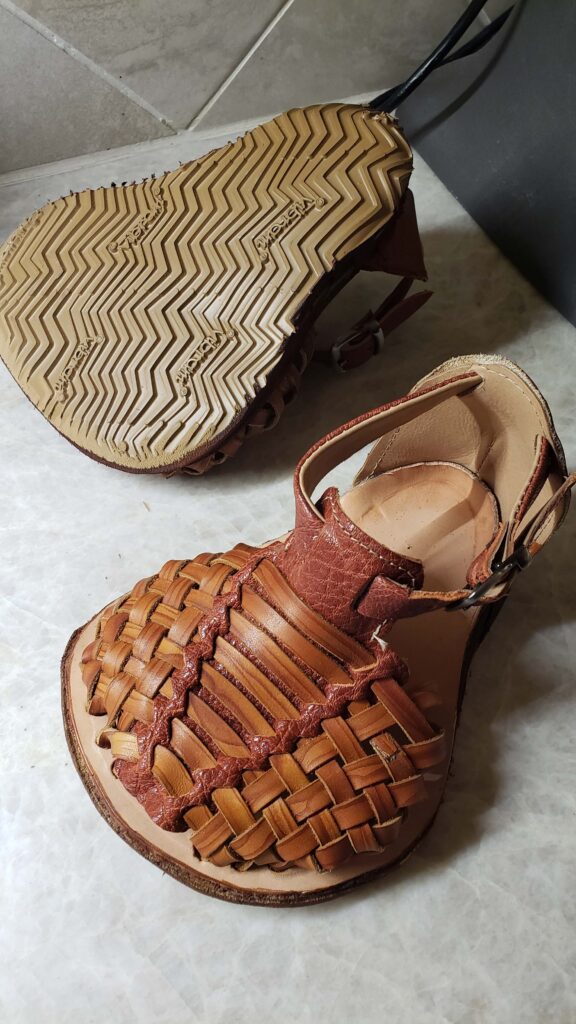 Close-up of a handcrafted leather sandal with intricate woven details, set against a light marble surface, showcasing craftsmanship.