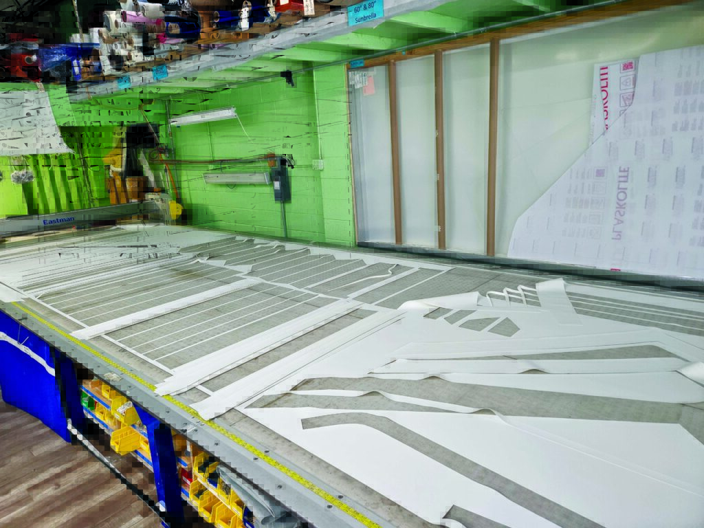 White fabric patterns laid out on a cutting table, surrounded by colorful rolls of materials and green walls.