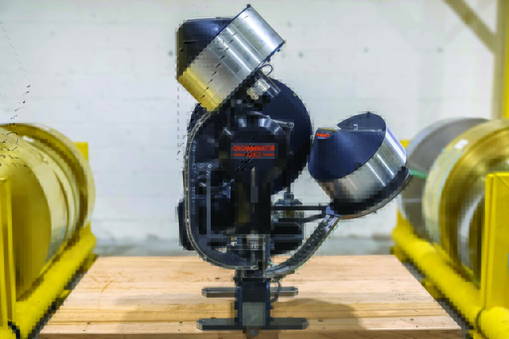Close-up of the GROMINATOR MK2, a dual-bladed marine cutting machine, on a wooden table with yellow benches in the background.