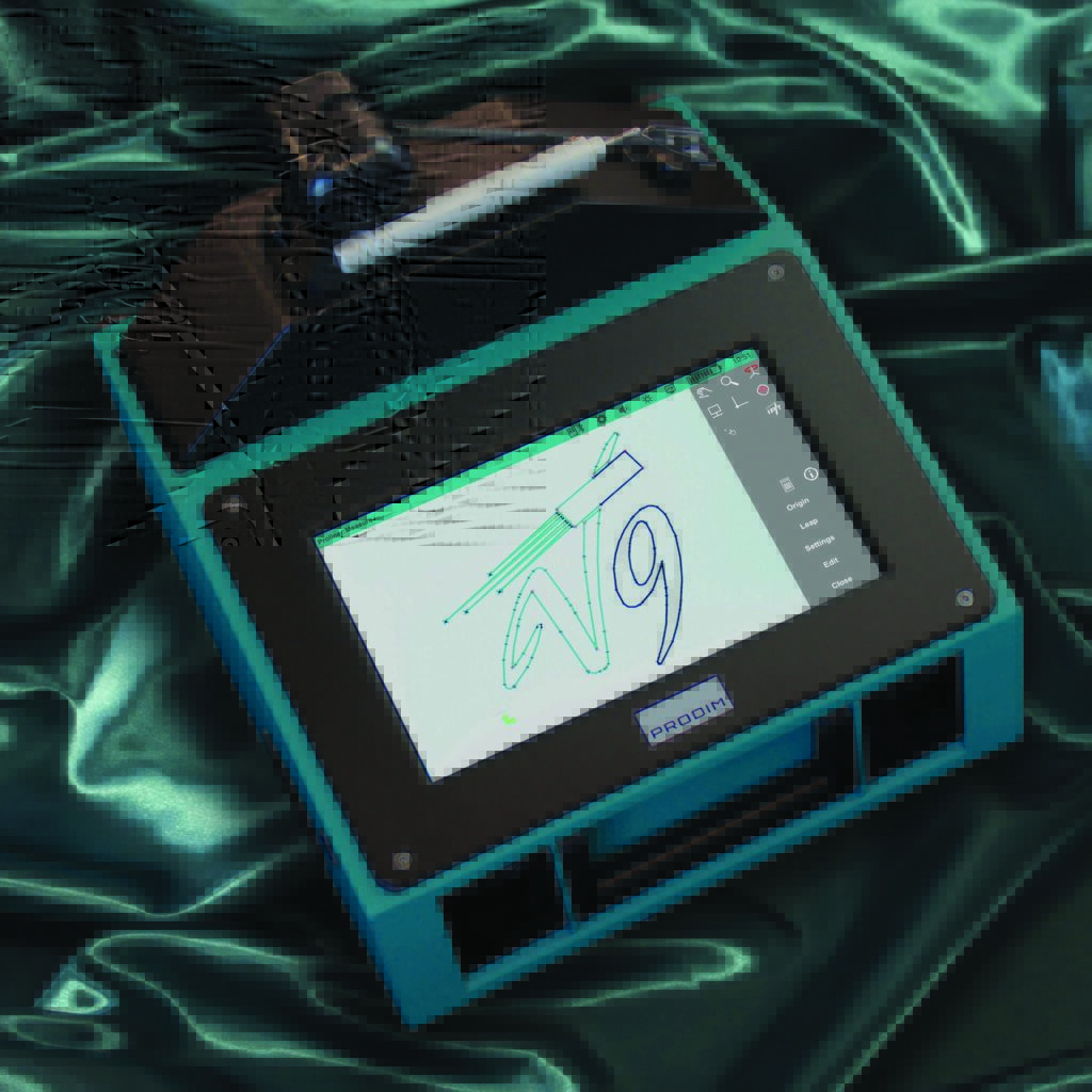 A teal Prodim Proliner V9 device with a touchscreen displaying a design on a glossy green fabric background.