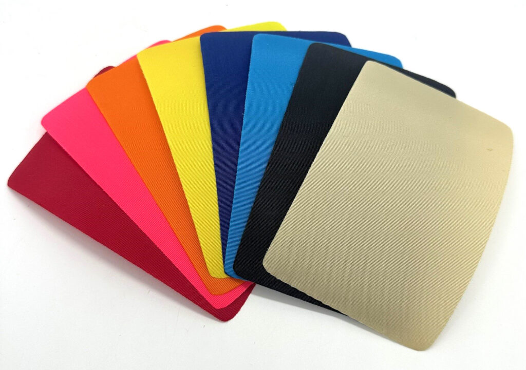 A fan of colorful fabric swatches in vibrant hues, including red, pink, orange, yellow, blue, black and beige, arranged in a gradient.