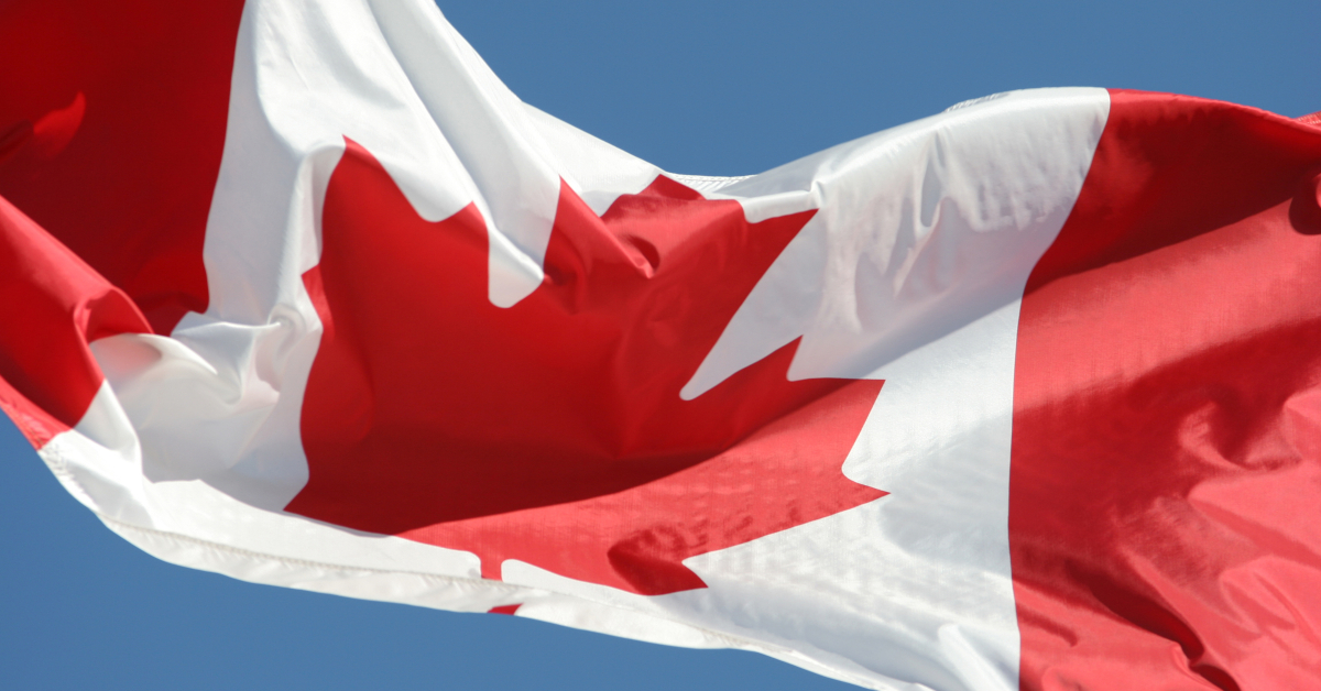 dreamstime_xxl_3579727_WP Canadian flag fluttering against a clear blue sky, prominently displaying the red and white colors with a central maple leaf emblem.