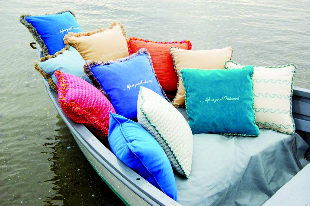 pillowsboat (2) Colorful pillows in various patterns and shades are arranged on the edge of a boat, resting on calm water.